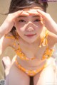 A woman in a yellow bikini sitting in the water.