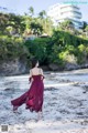 A woman in a red dress walking on a beach.