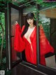 A woman in a red robe is looking out of a window.