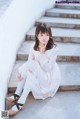 A woman sitting on the steps of a building wearing a white dress.