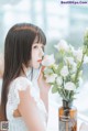 A woman in a white dress smelling a vase of flowers.