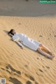 A woman in a white dress laying on a sand dune.