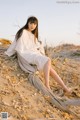 A woman in a white dress sitting on a tree branch.