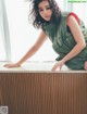 A woman leaning on a wooden table in front of a window.