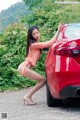 A woman leaning against a red car on the side of the road.