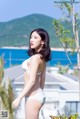 A woman in a white bikini standing next to a tree.