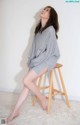 A woman sitting on a stool wearing a grey sweatshirt dress.