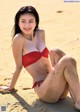 A woman in a red bikini sitting on a sandy beach.