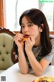 A young woman sitting at a table eating a piece of food.