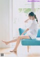 A woman sitting on a blue couch in front of a window.