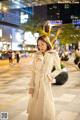 A woman in a white trench coat is walking down the street.