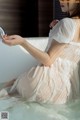 A woman in a white dress sitting in a bathtub.