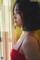 A woman in a red bra looking out a window.