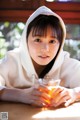 A woman in a white hoodie holding a glass of tea.